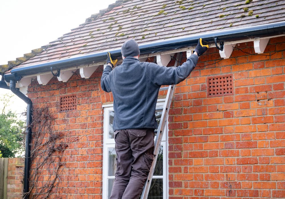Person on ladder fixing house gutter.