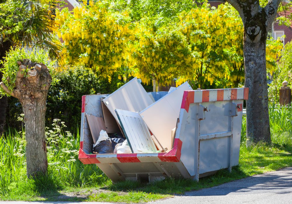 Dumpster with debris near blooming trees.